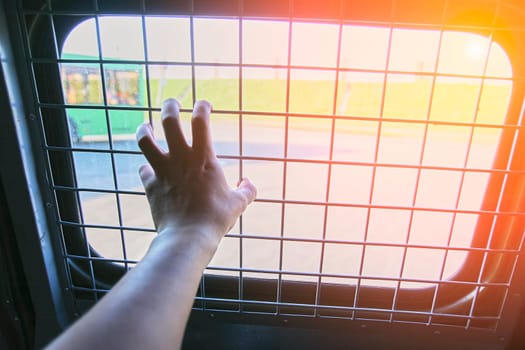 Man in prison hand holding a steel cage prison bars. criminal criminal is locked in prison. The hand of a detained man in a police car.