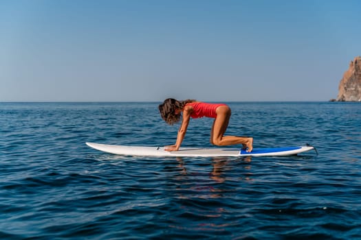 Sporty girl on a surfboard in the sea on a sunny summer day. In a red swimsuit, she sits in the splits on the sap. Summer entertainment on Stortom by the sea.