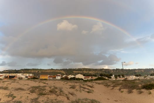 Rainbow over the village on cloudy sky. Mid shot