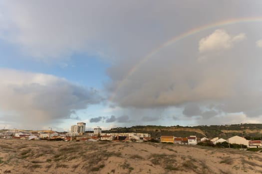 Rainbow over a town on cloudy sky. Mid shot