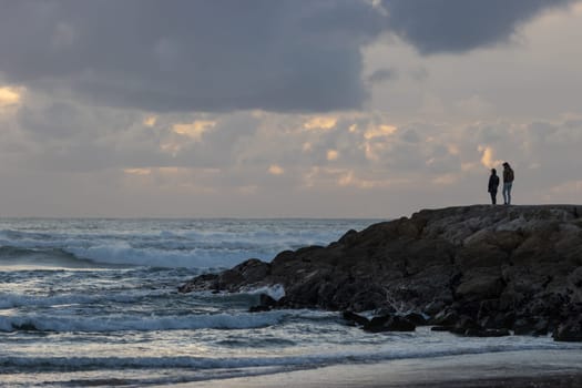 A couple standing on the rock by the storm sea. Mid shot