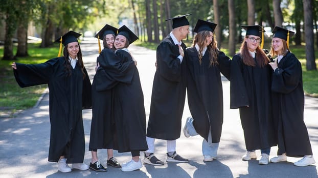 Group of happy graduates in robes hugging outdoors