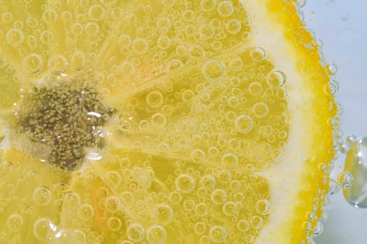 Slice of ripe lemon in water on white background. Close-up of lemon in liquid with bubbles. Slice of ripe citron in sparkling water. Macro image of fruit in carbonated water