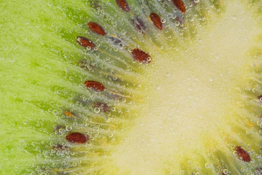 Close-up of a kiwi fruit slice in liquid with bubbles. Slice of ripe kiwi fruit in water. Close-up of fresh kiwi slice covered by bubbles. Macro horizontal image