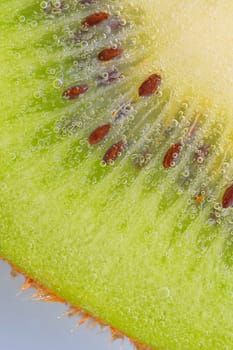 Close-up of a kiwi fruit slice in liquid with bubbles. Slice of ripe kiwi fruit in water. Close-up of fresh kiwi slice covered by bubbles. Macro vertical image