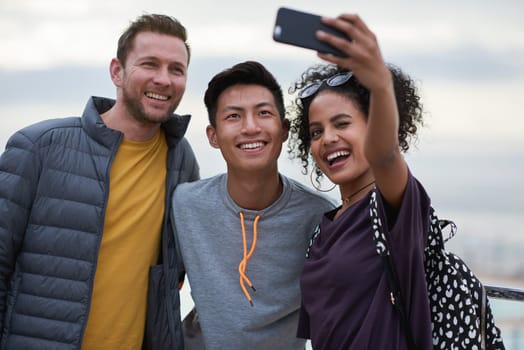 Men, black woman and friends selfie at beach for holiday travel, together and smile for internet blog post. Outdoor adventure, phone and profile picture for social media app by ocean with diversity.