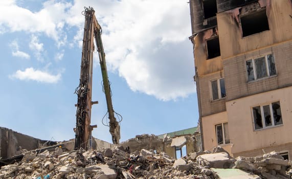 Excavator with hydraulic crusher at the demolition of a residential building. City renewal. Dismantling, destruction of a high-rise multi-storey building for reconstruction. Debris clearing