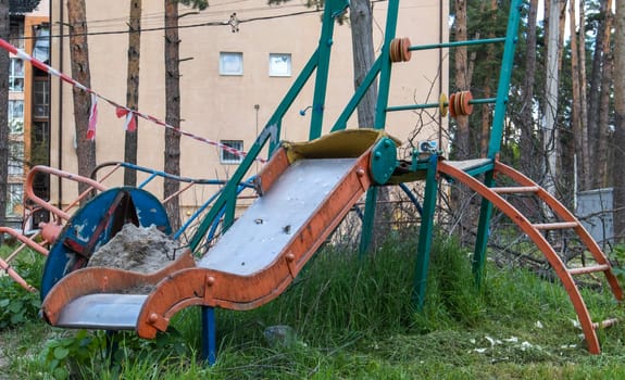 Affected after the bombing of multi-storey residential buildings. A playground was destroyed in front of the ruins of the house. The concept of war in Ukraine. Consequences of a missile strike