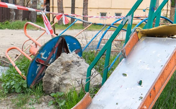 Affected after the bombing of multi-storey residential buildings. A playground was destroyed in front of the ruins of the house. The concept of war in Ukraine. Consequences of a missile strike