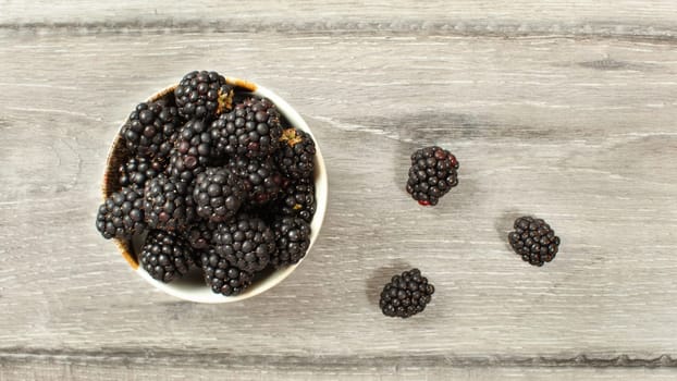 Top down view, small bowl with blueberries some of them spilled on desk.