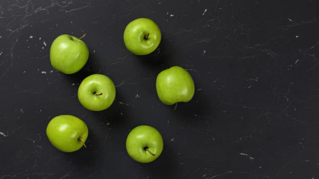 Top down view, 6 green apples on dark marble board. Space for text on right side.