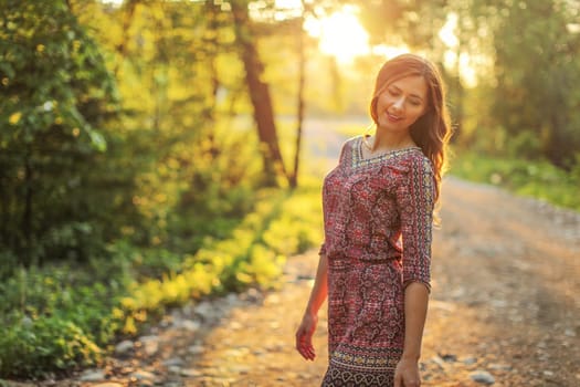 Young woman on forest path, looking down over her shoulder sun behind her, backlight creates nice bokeh in background.