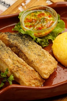 Whole fried fish in a red plate served with mamaliga and garlic souce