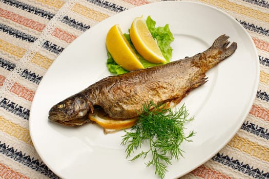 Whole fried fish in a white plate with lemon