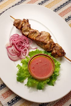 Grilled pork kebab with red onion and chilly souce on a white plate