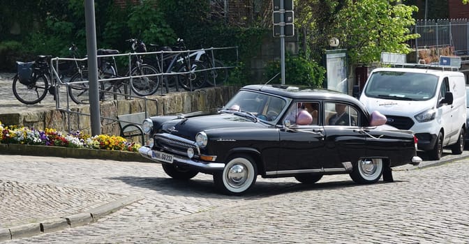 Bad Bentheim, Germany - May 5 2023 A couple is driven to their wedding ceremony in a black old-timer from Russia. The car is a GAZ Volga 2nd generation: the Shark with a jumping deer on the hood