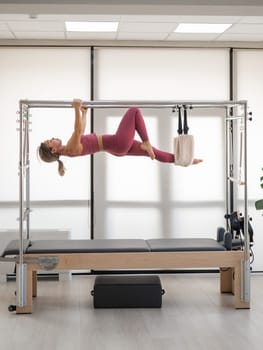 Beautiful asian woman in pink sportswear doing pilates on bed reformer