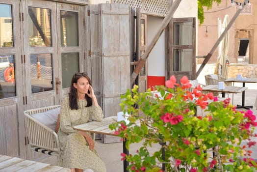 A young woman sits in a street cafe and enjoys the views of the old city of the Emirates. Deira, Burdubai