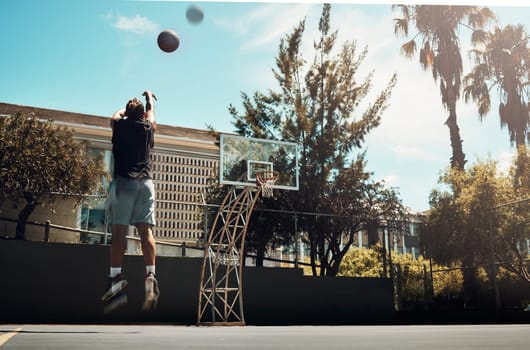 Basketball, outdoor and a man shooting ball alone on basketball court in Miami summer sun. Fitness, training and health, basketball player jumping to score on court at weekend sports game practice