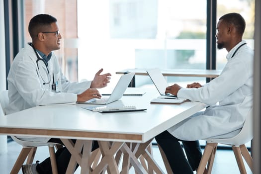 Healthcare, strategy and planning, doctors in meeting with laptop and discussion at table in hospital meeting room. Teamwork, collaboration and innovation in medical research, men talking in clinic