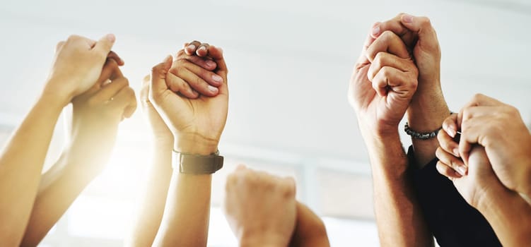 Closeup shot of a group of unrecognizable businesspeople holding hands while raising their arms.