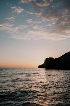 A red burning sunset with the silhouette of a cliff over the sea. Abstract nature summer or spring ocean sea background. Small waves on golden warm water surface with bokeh lights from sun.