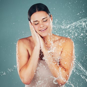 Water, splash and cleaning with a woman in studio on a blue background for hygiene or hydration in the shower. Spa, wellness and beauty with an attractive young female washing in the bathroom.