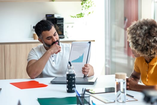 Mid adult indian boss man in the office showing coworkers market tendencies graph. Copy space. Business meeting concept.