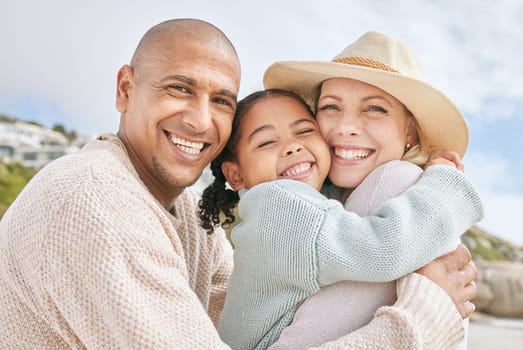Mom, dad and child hug at the beach on family vacation, holiday and enjoying weekend. Love, affection and multicultural parents with happy girl in portrait smile, bond and embrace by ocean together.