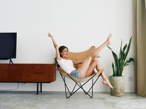 Woman lying in a leather armchair raised arms and legs cheerful happiness and a smile, relaxing at home stylish modern interior with white walls, copy space. High quality photo