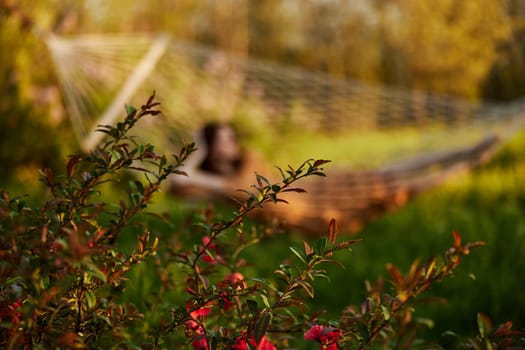 a beautiful woman is resting in nature lying in a mesh hammock in a long orange dress looking to the side, propping her head with her hand. Horizontal photo without focus. High quality photo