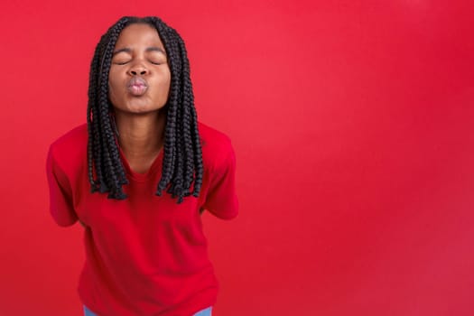 African woman blowing a kiss with eyes closed in studio with red background