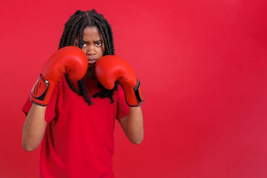 African woman with boxing gloves in fight pose in studio with red background