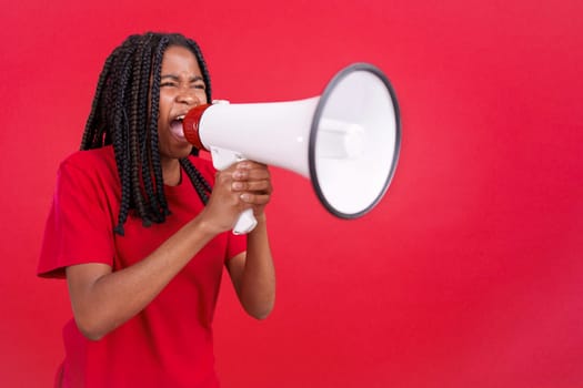 Angry african woman standing and using a megaphone in studio with red background