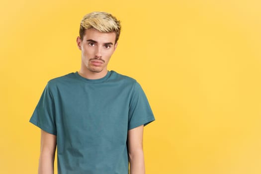 Sad gay man standing and looking at camera in studio with yellow background