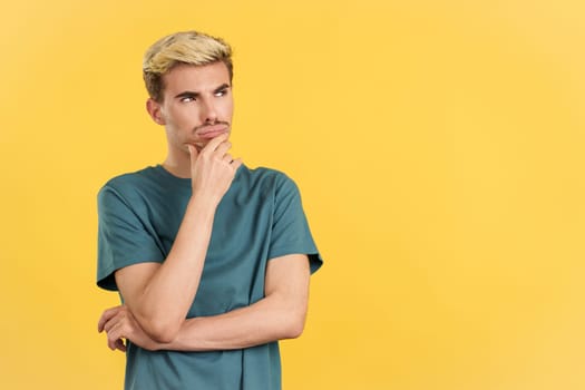 Gay man with hand on face and thoughtful expression in studio with yellow background