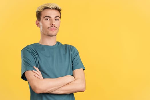 Relaxed gay man standing whit arms crossed looking at camera in studio with yellow background