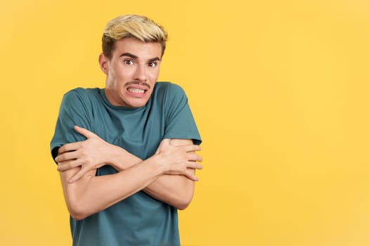 Gay man looking at camera gesturing he is cold in studio with yellow background