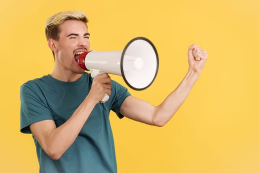 Angry gay man yelling using a megaphone in studio with yellow background