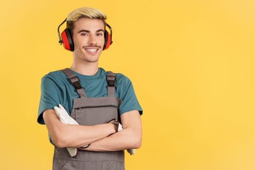 Friendly gay man carpentry worker in work uniform in studio with yellow background