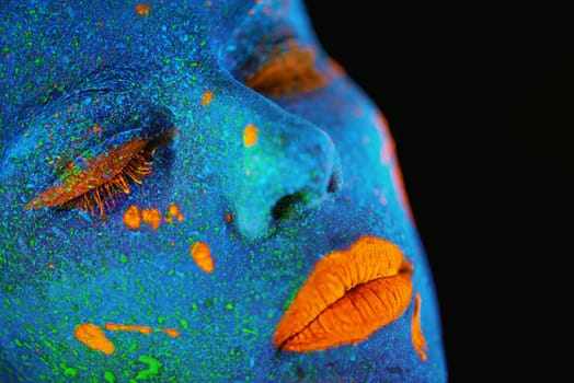 Neon paint, makeup and woman face closeup with dark background and creative cosmetics. Surreal glow, fantasy and psychedelic cosmetic of a female model with unique and creativity art in studio.