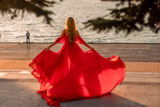 Sunrise red dress. A woman in a long red dress against the backdrop of sunrise, bright golden light of the sun's rays. The concept of femininity, harmony