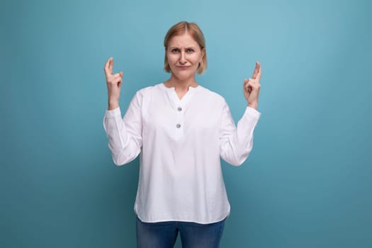 stylish blond middle-aged woman in a white blouse demonstrates something on a studio background with copyspace.