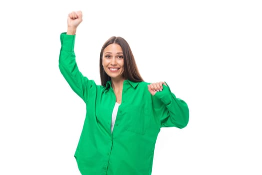 smiling cheerful young caucasian brunette lady with makeup dressed in a green shirt and jeans on a white background with copy space.