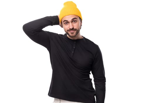 successful 30s authentic brunet male adult in black sweater and yellow cap on white background with copy space.