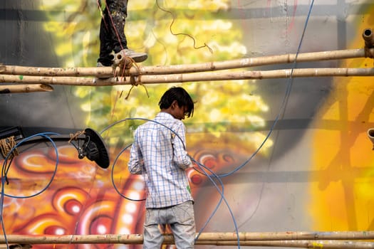 Haridwar, India - circa 2023: man standing on bamboo scaffolding using a spray air gun to paint a picture of hanuman the hindu god on janaki setu bridge in rishikesh India