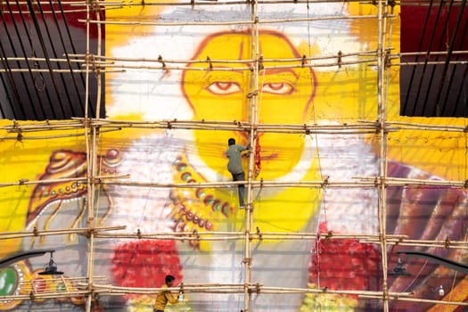 Haridwar, India - circa 2023: man standing on bamboo scaffolding using a spray air gun to paint a picture of hanuman the hindu god on janaki setu bridge in rishikesh India