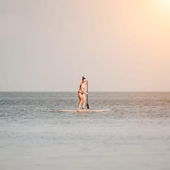 Sea woman sup. Silhouette of happy middle aged woman in rainbow bikini, surfing on SUP board, confident paddling through water surface. Idyllic sunset. Active lifestyle at sea or river
