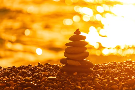 Balanced rock pyramid on pebbles beach. Golden sea bokeh on background. Selective focus, zen stones on sea beach, meditation, spa, harmony, calm, balance concept