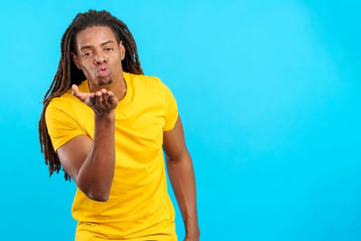 Latin man with dreadlocks blowing a kiss in studio with blue background